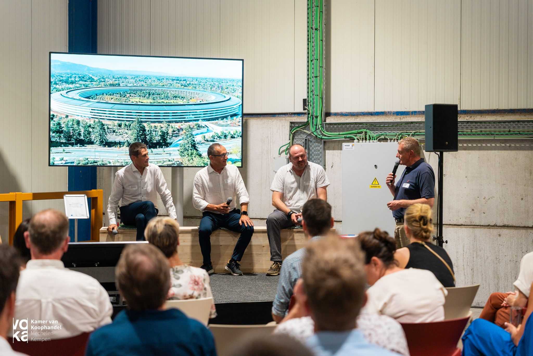 Een panel van drie experts zit voor een scherm met een afbeelding van het Apple-hoofdkwartier in Cupertino, Calfornië
