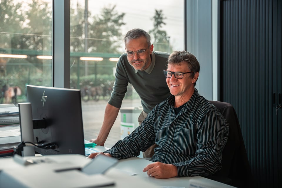 Twee personen kijken lachend naar een computerscherm