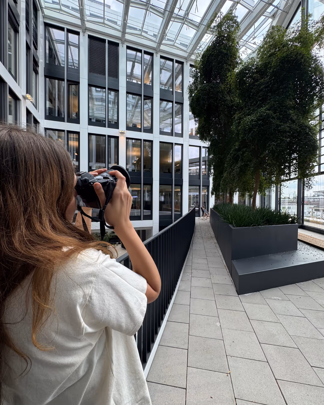 Frau fotografiert Glasgebäude mit grünen Pflanzen und Dachverglasung