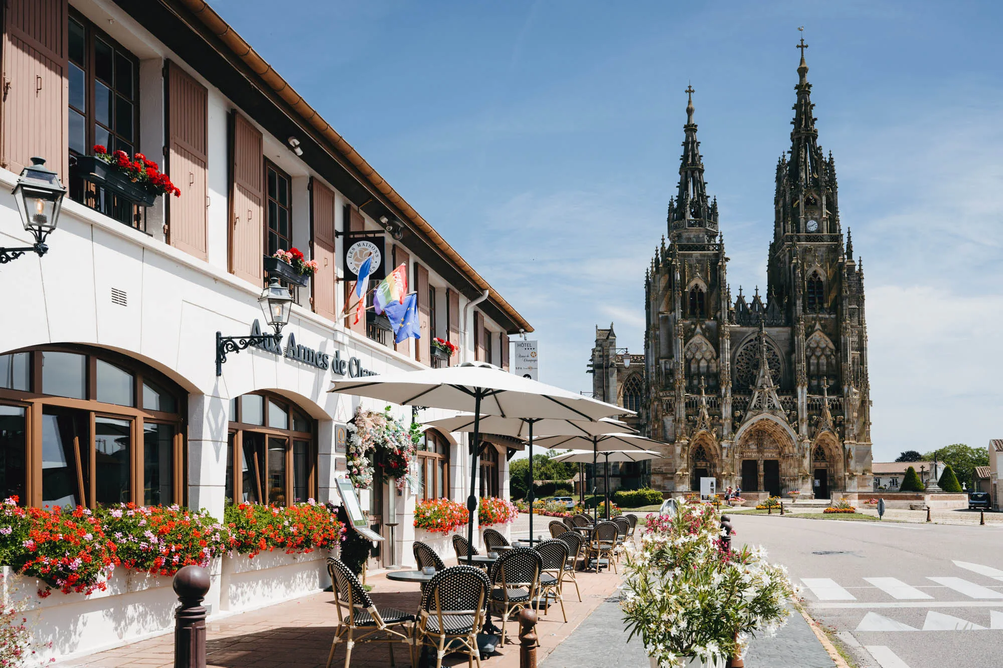 Façade de l’hôtel Aux Armes de Champagne avec terrasse fleurie, face à la Basilique Notre-Dame de l’Épine, classée au patrimoine mondial de l’UNESCO