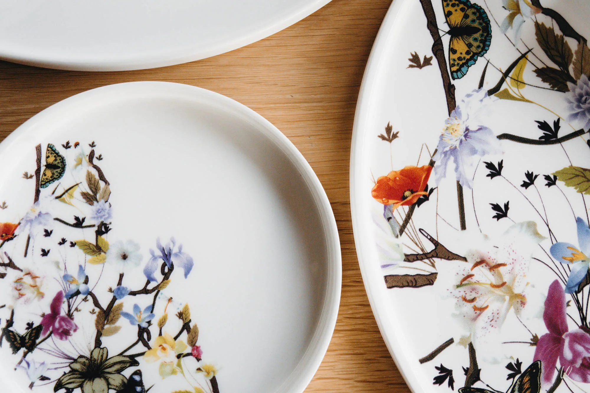 Assiettes en porcelaine aux motifs floraux et papillons, posées sur une table en bois – Détail de l’art de la table au Restaurant Cuvée 31 à l’hôtel Aux Armes de Champagne