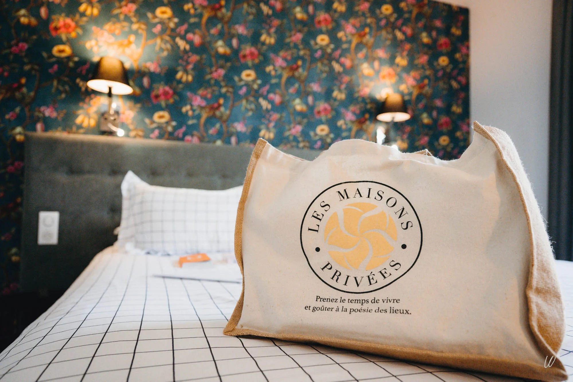Panier de bienvenue “Les Maisons Privées” posé sur un lit à l’hôtel Les Armes de Champagne, symbole d’un accueil attentionné et personnalisé.