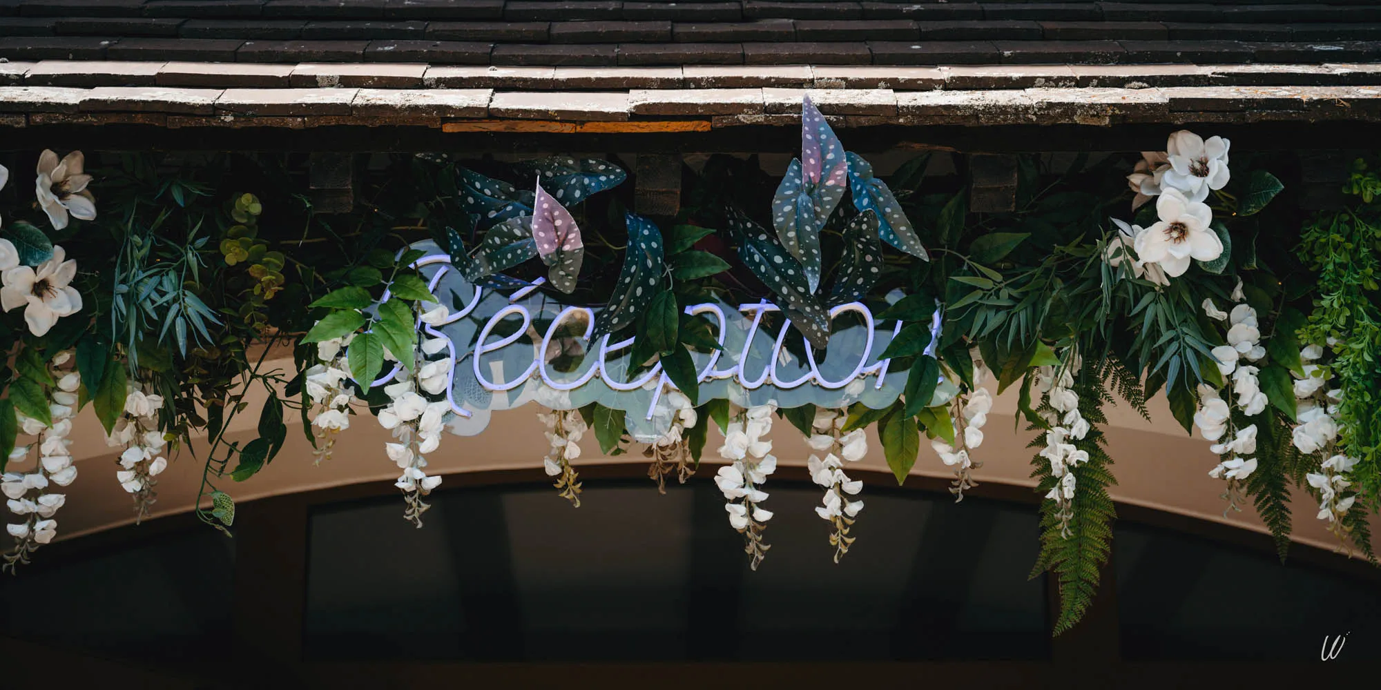 Enseigne "Réception" en néon entourée de fleurs blanches et feuillage décoratif à l'entrée de l'hôtel Armes de Champagne.