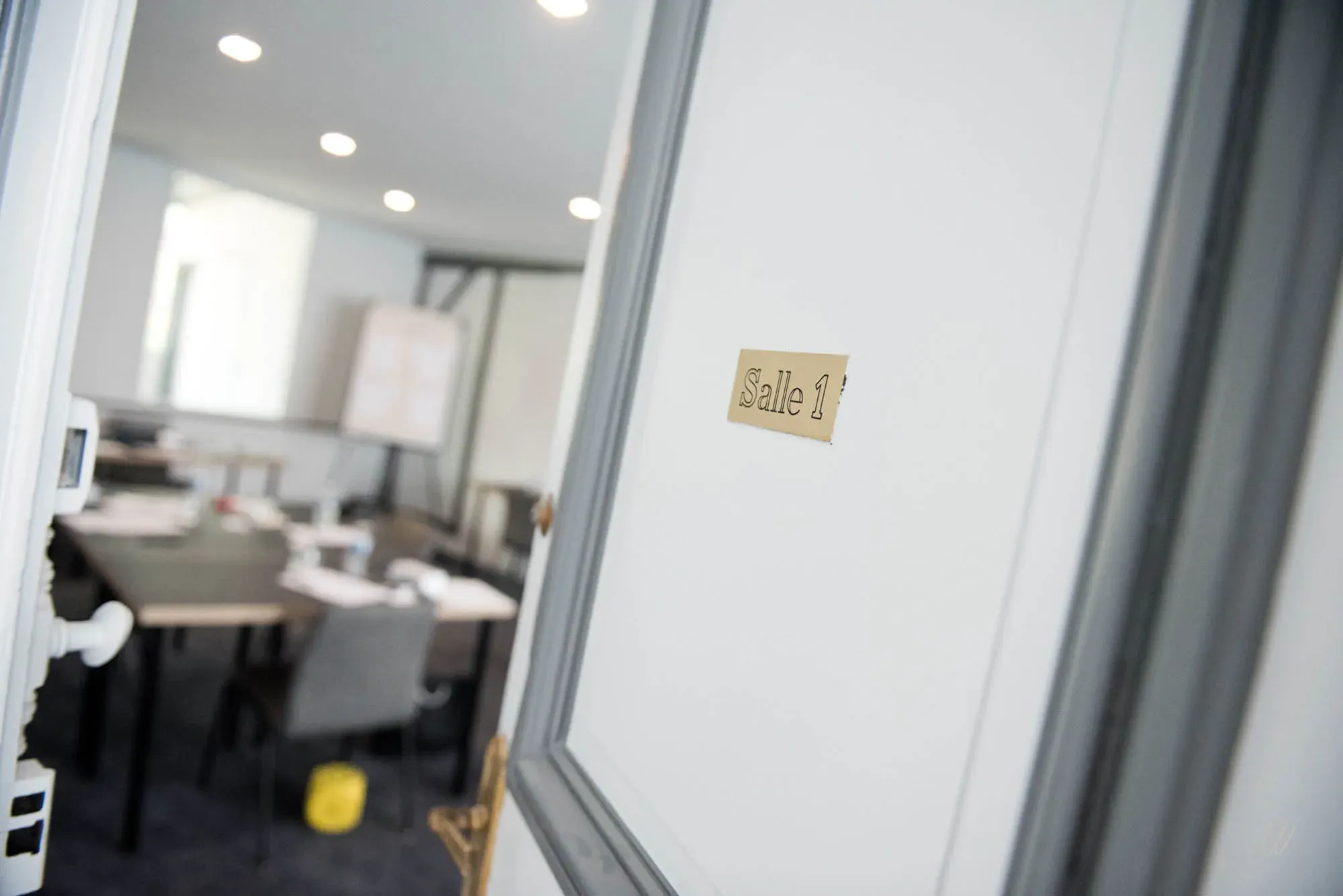 Porte entrouverte de la Salle 1 de l’hôtel Les Armes de Champagne, donnant sur un espace de réunion moderne et lumineux, idéal pour les séminaires d'entreprise.