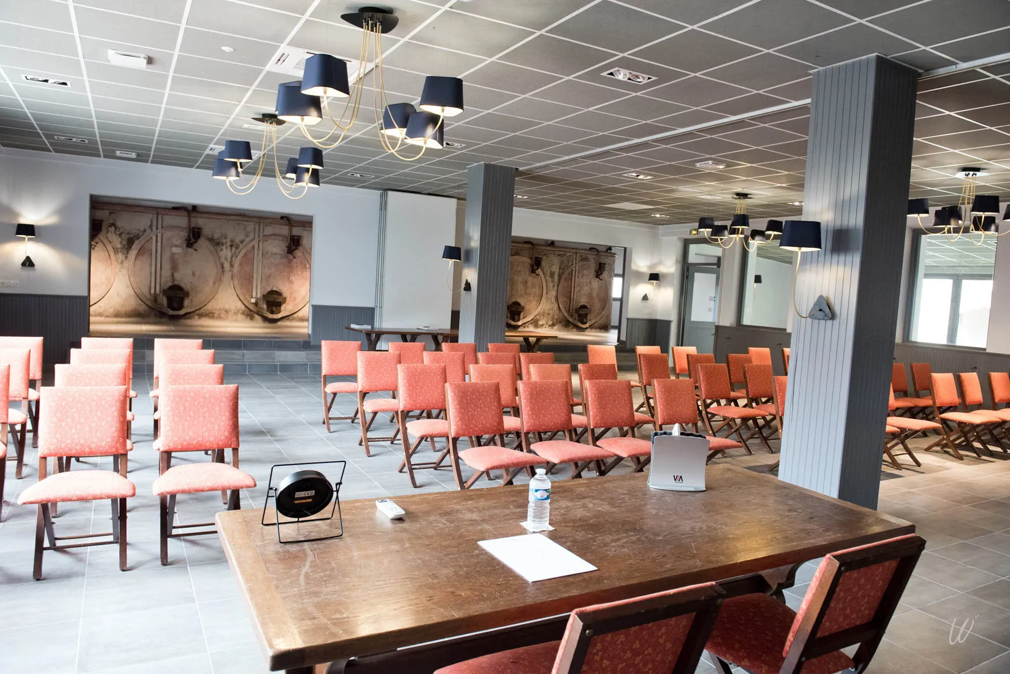 Salle de conférence spacieuse à l’Hôtel Les Armes de Champagne, équipée de rangées de chaises rouges, d’un bureau pour les intervenants et de décors muraux évoquant des fûts de vin, idéale pour séminaires, réunions ou présentations professionnelles.