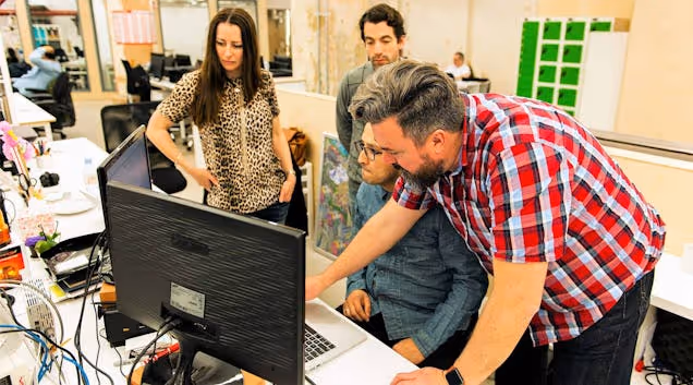 4 individuals working together on computers in a workspace