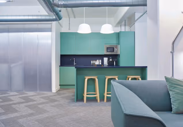An image of a green kitchen, a couch arm in the Fora breakout space.