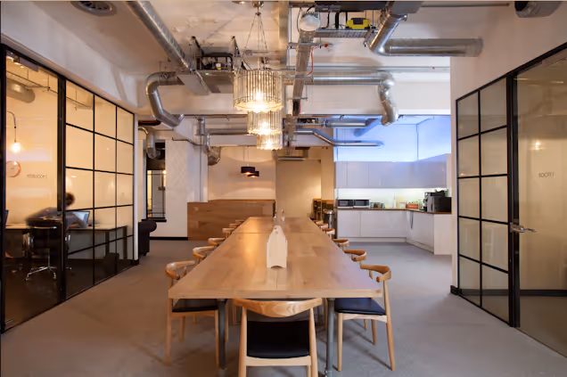 An image of a large table in a communal space and a kitchen in the background.