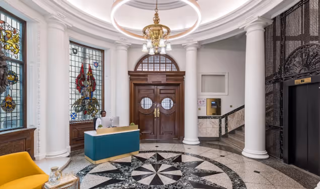 A photo of the grand entrance with stained glass windows and a receptionist at a desk.