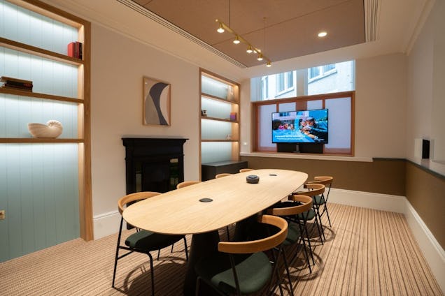Room featuring an oval wooden table, a black fireplace, back-lit recessed shelving, and a wall-mounted screen.