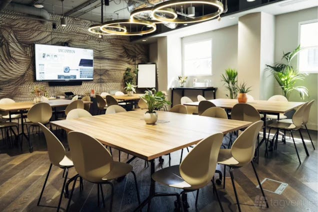Coworking space with wooden square tables, tear-drop chairs, gold halo pendant lights, and a graphic wave-patterned feature wall.