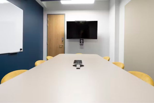 Room with a white table, yellow chairs, a TV display screen, and blue and white walls