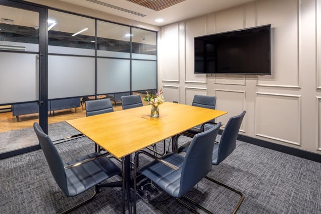 Meeting room with a light wooden table with flowers in the centre and blue chairs surrounding the table.