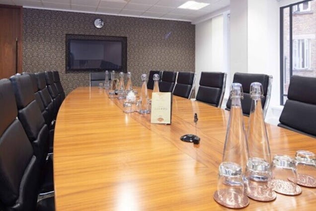 Room with black long office chairs with a wooden table that has multiple glass bottles on top