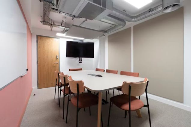 Meeting room with a pink accent wall, terracotta-colored chairs, acoustic wall panels, and an industrial ceiling with exposed ductwork.