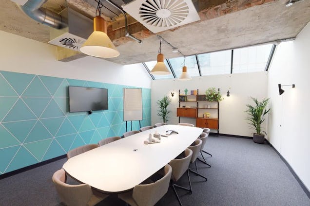 Meeting room with an oval table, geometric teal wall, slanted skylight window, and mid-century modern shelving.
