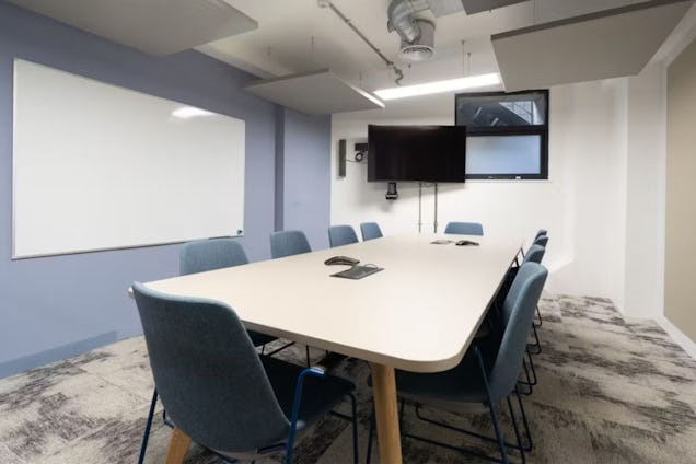 Meeting room with a long white table, blue fabric chairs, and a whiteboard on a periwinkle wall