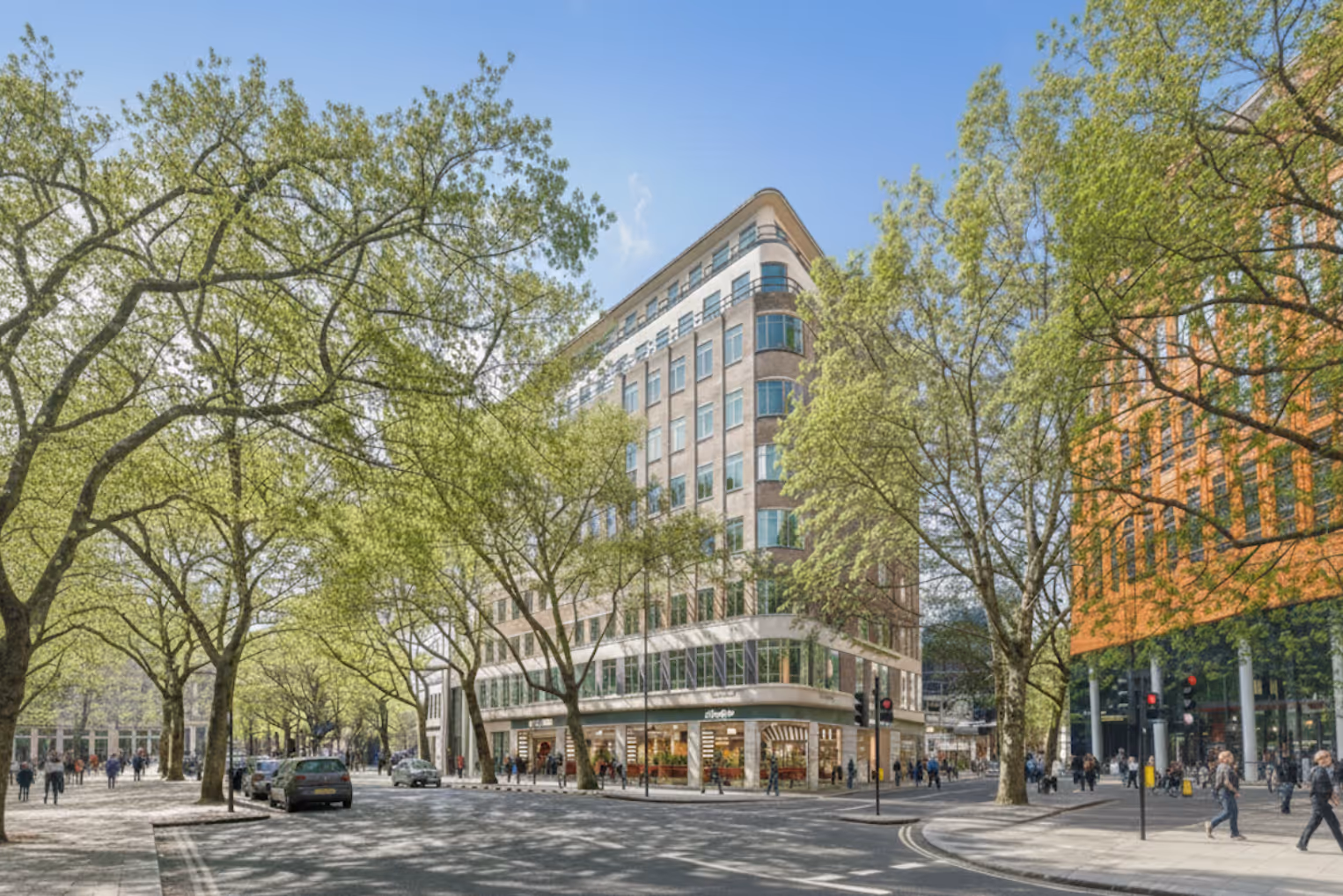 Corner view of a modern multi-story office building on a sunlit London street, framed by large leafy green trees and wide pavements