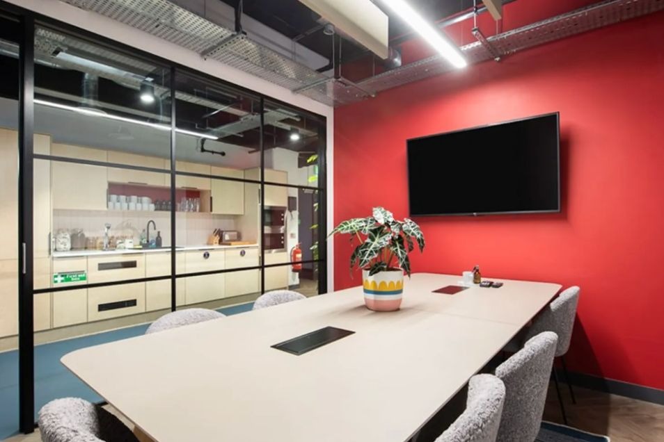 Modern office meeting room with red wall, glass kitchen, and white table at Runway East Borough Market