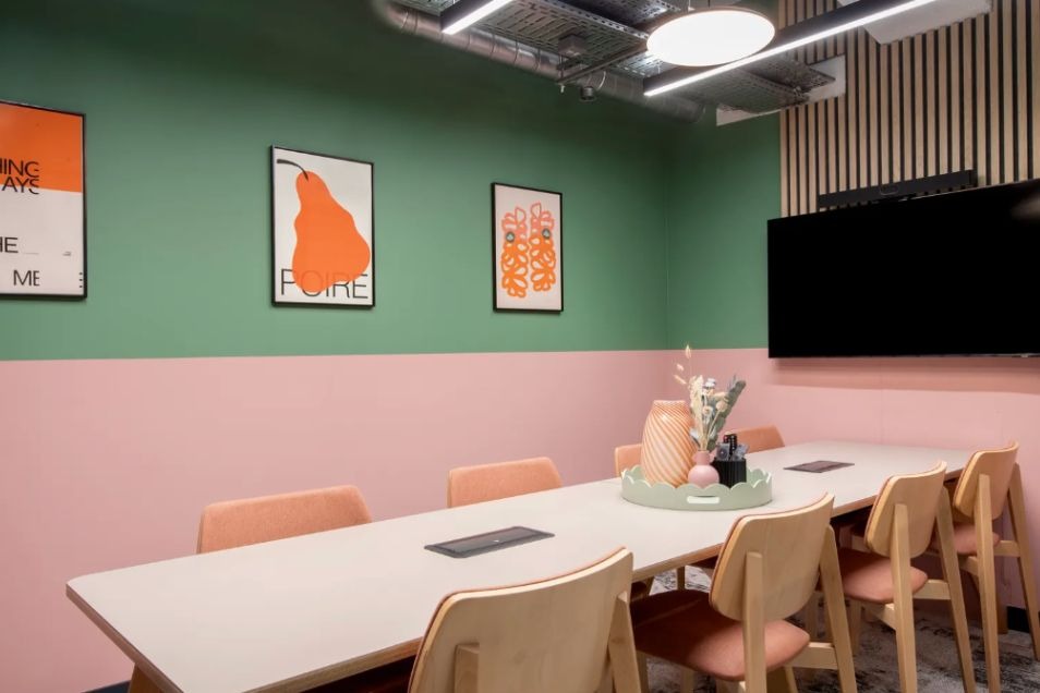 Modern meeting room with green walls, pink base, orange art, and white table at Runway East London Bridge