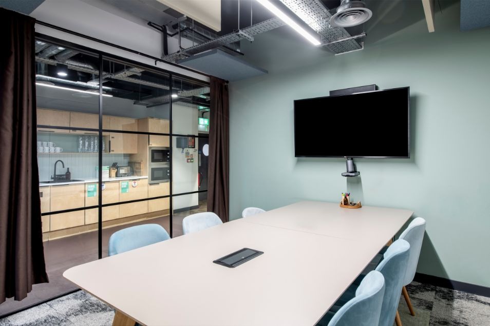 Modern meeting room with glass partition, white table, and blue chairs at Runway East Borough Market