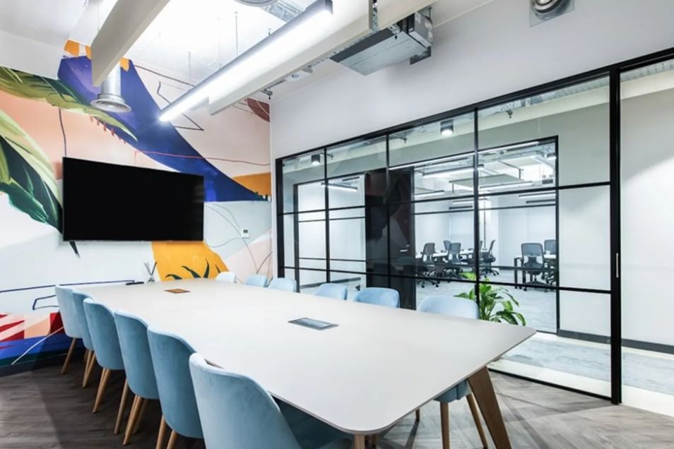 Modern meeting room with blue chairs, white table, and glass partition at Runway East London Bridge