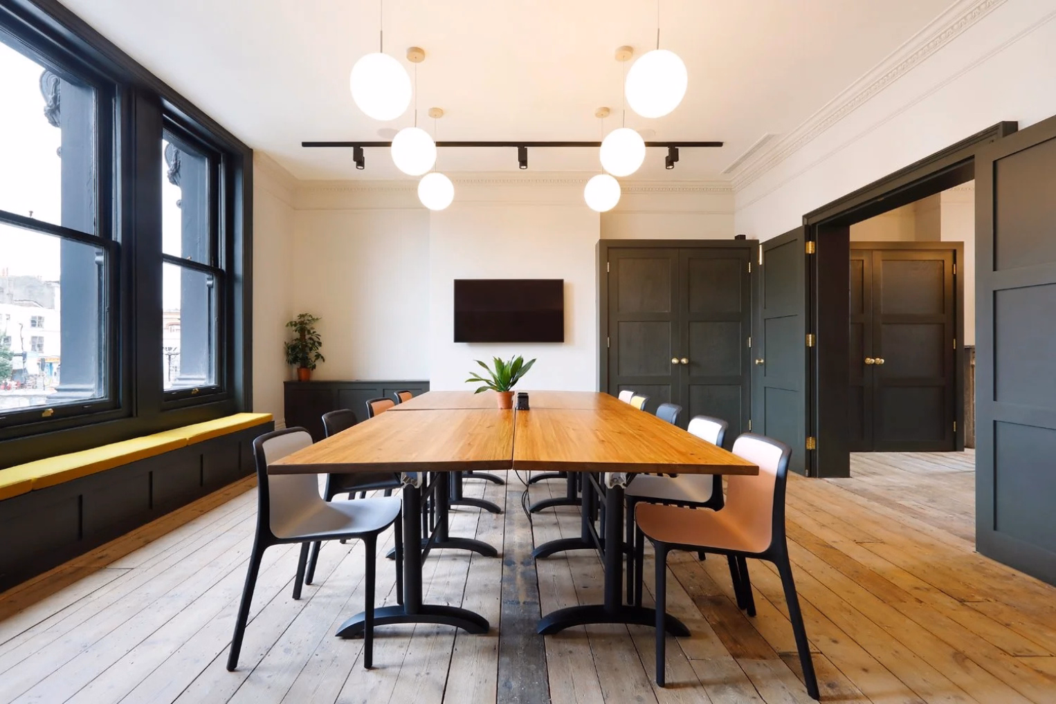 A light-filled meeting room with a wooden table, globe pendant lights, and dark panelled doors against original floorboards.