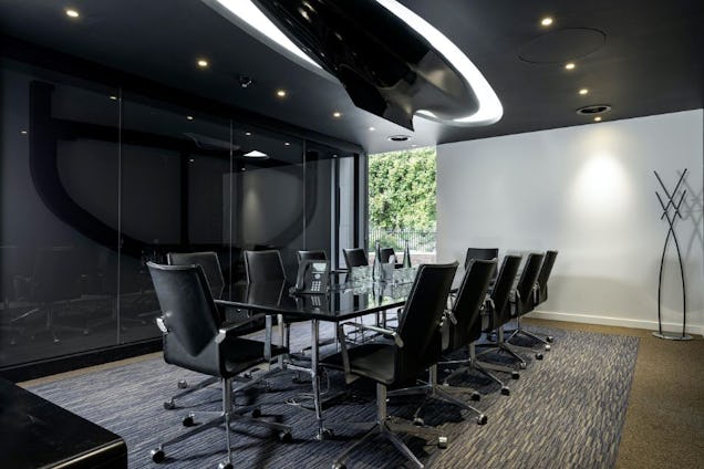 Boardroom with a glass table, black executive chairs, a dark reflective ceiling with curved light features, and a large frosted glass partition.