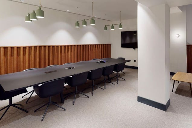 Boardroom featuring a long black table, dark swivel chairs, wood-slatted wall panelling, and green pendant lighting.