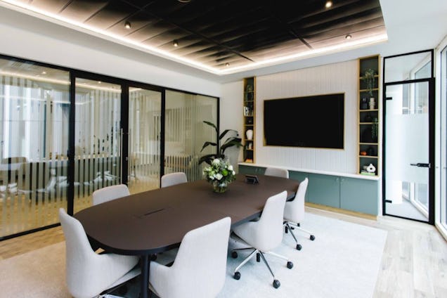 Boardroom with an oval dark wood table, white swivel chairs, glass-partitioned walls, and an integrated media unit.