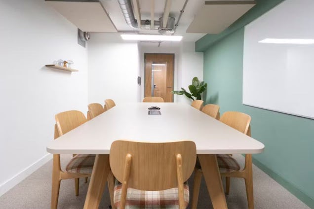 Meeting Room with a light grey table, wooden chairs with plaid upholstery, a sage green accent wall, and a large whiteboard.