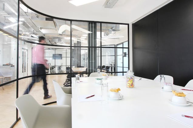 Meeting room with a white table and chairs, enclosed by a curved black-framed glass partition wall.
