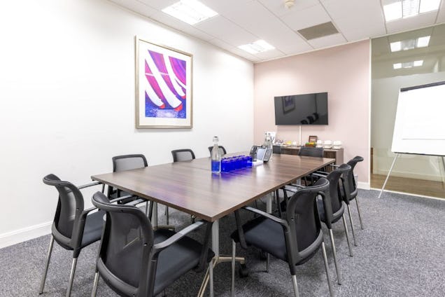 Professional meeting room with a dark wood table, black mesh chairs, framed purple wall art, and a wall-mounted TV.