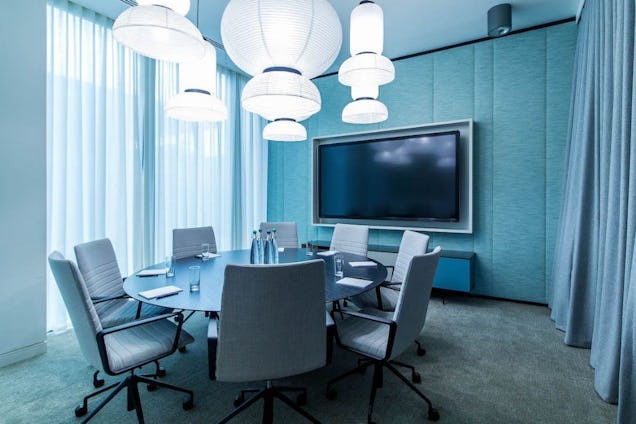 Meeting room with a round table, grey swivel chairs, light blue acoustic walls, and large white sculptural pendant lights.