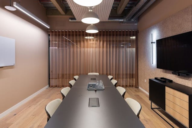 Boardroom with a long dark table, cream chairs, light wood floors, and floor-to-ceiling brown sheer curtains.