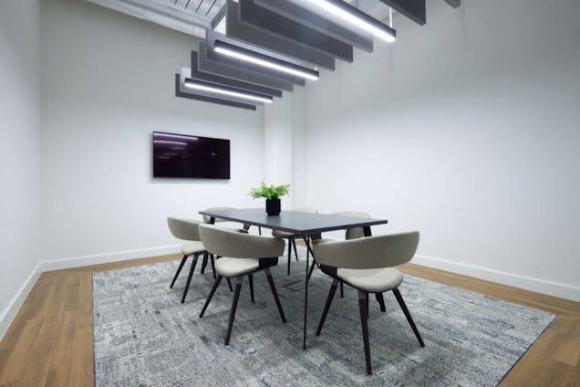 Minimalist meeting room with a dark table, beige bucket chairs, a grey patterned rug, and linear ceiling lights.