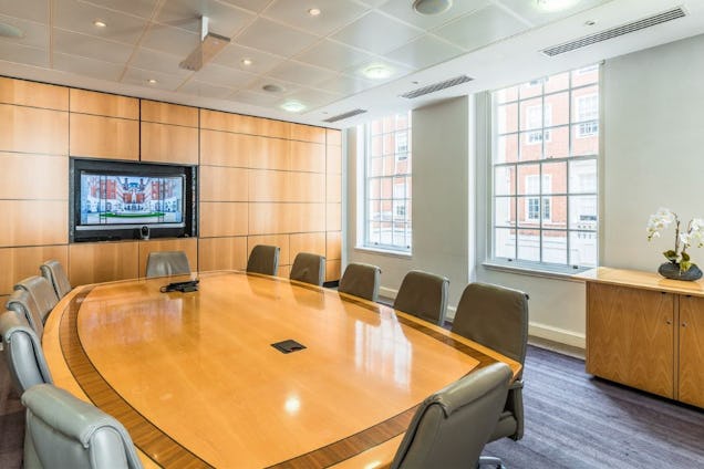 Boardroom with a polished wood oval table, grey leather chairs, wood-panelled walls, and tall sash windows.