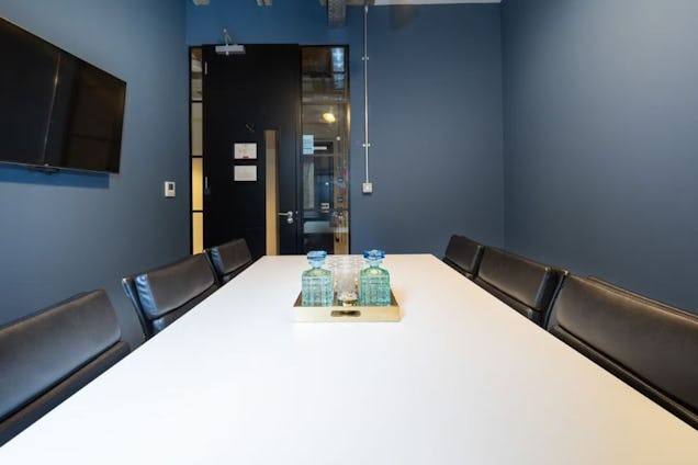 Small meeting room with slate blue walls, a white table, black chairs, and a gold tray with water decanters.