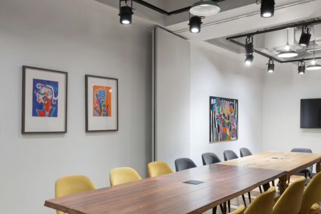 Boardroom with a long wood table, yellow and grey chairs, industrial track lighting, and colourful abstract wall art.