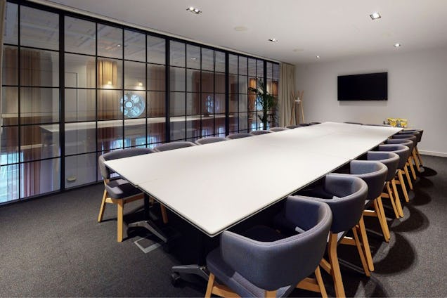 Boardroom with a long white table, grey tub chairs with wood legs, and a black-framed glass partition wall.