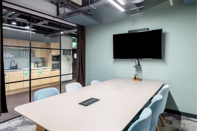 Meeting room with light blue chairs, a white table, and a glass partition wall looking into a kitchenette.