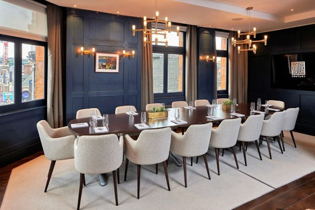 Boardroom with navy wood-panelled walls, a long dark table, cream upholstered chairs, and modern gold chandeliers.