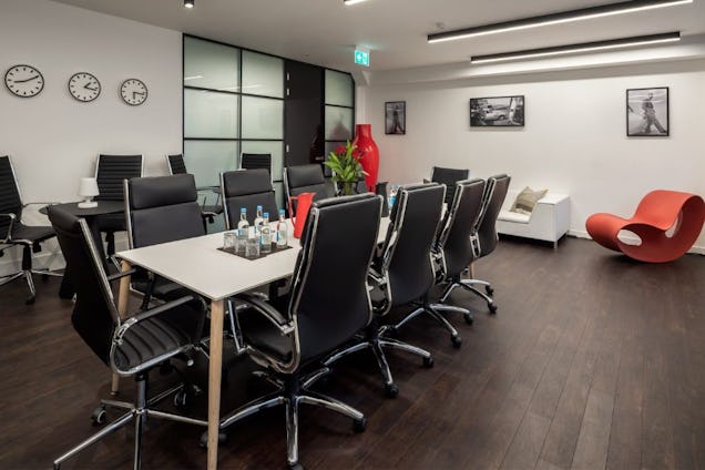 Spacious meeting room with a white table, black leather chairs, dark wood flooring, and a unique orange sculptural lounge chair.