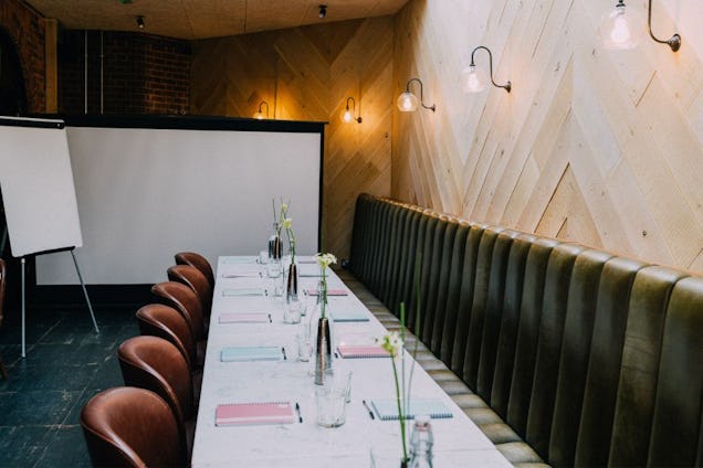 Meeting space with a long white table, brown leather chairs, a green velvet banquette, and a chevron-patterned wood wall.