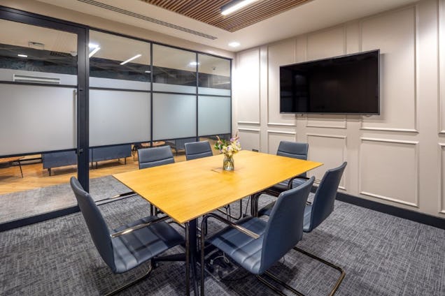 Meeting room with a light wood table, grey chairs, panelled walls, and a glass partition wall.
