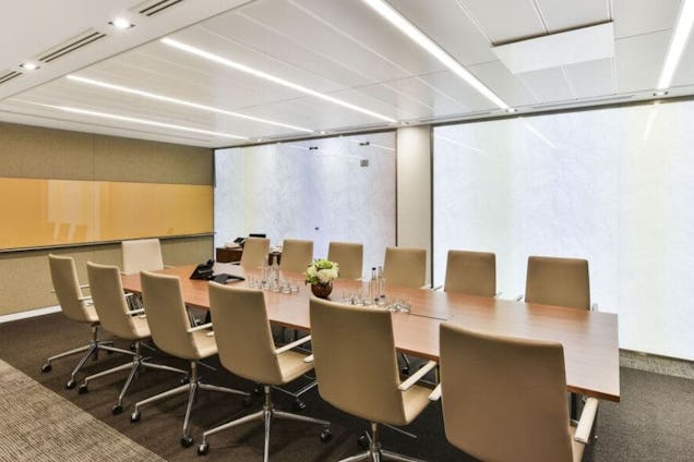 Boardroom with a long wooden table, tan leather rolling chairs, and large backlit frosted glass wall panels.
