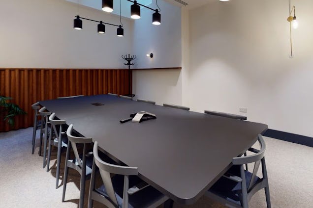 Minimalist meeting room with a large black table, grey wishbone chairs, wood-slat wainscoting, and black pendant lights.