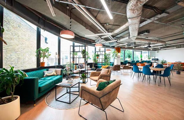 Open-plan office with teal sofas, lounge seating, long desks and large windows letting in plenty of natural light.