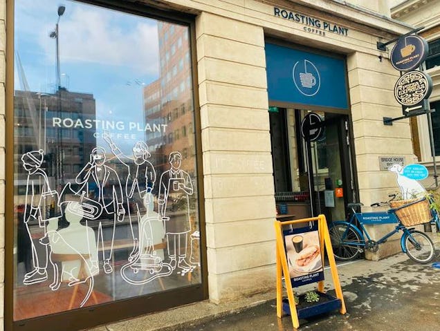 Shopfront with illustrated window display and signage, with a bicycle parked outside and a small pavement sign.