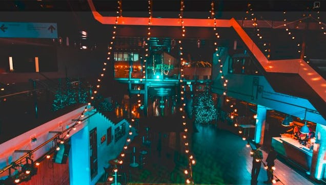 Large indoor venue with colourful lighting, string lights and multiple levels, set up for an evening event or gathering.
